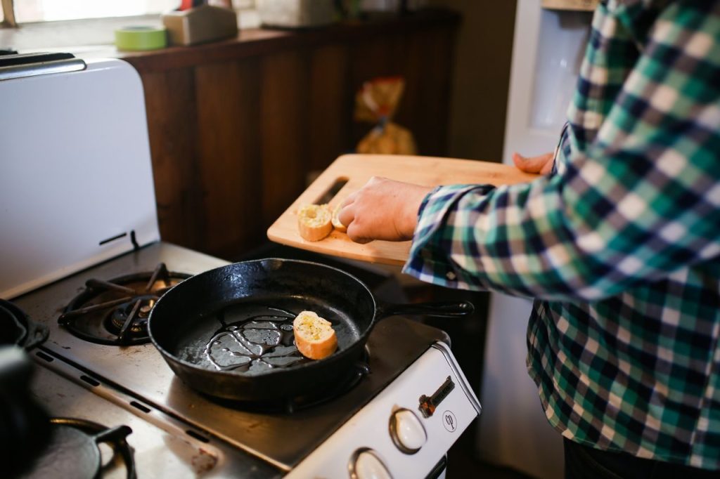 A person holding a frying pan while cooking at a stove